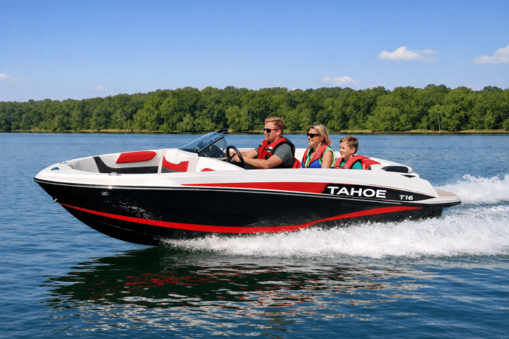 Family on a red and black boat named Tahoe T16 cruising on a lake with trees in the background.