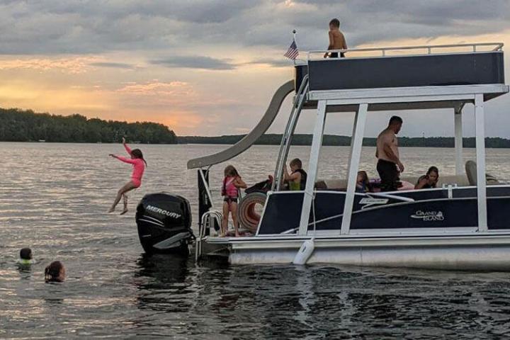 People enjoying a pontoon boat on a lake with a slide, during sunset.