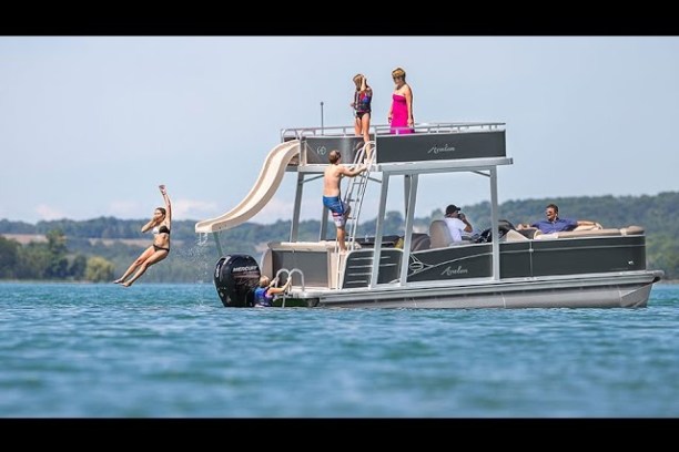 People on a pontoon boat with a slide; one person slides into the water.