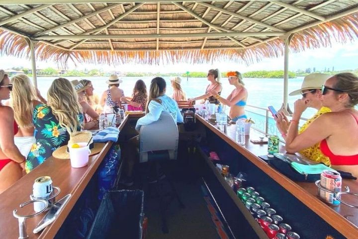 People enjoying drinks under a tiki hut on a boat, with a view of the water.
