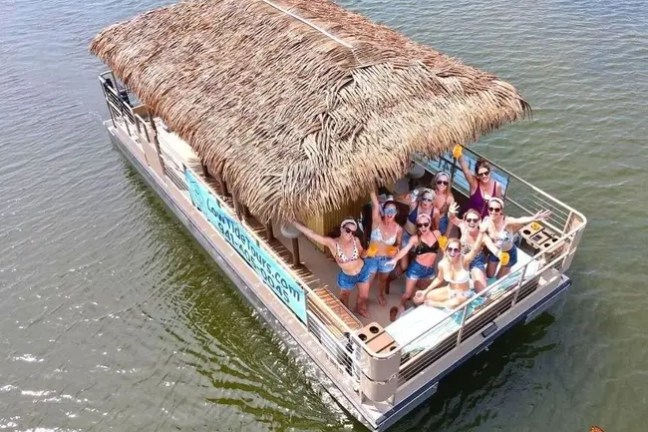 Group of people on a tiki boat in open water, waving and smiling.